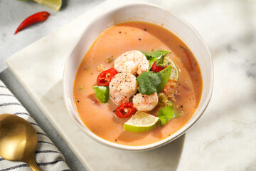 a spicy thai coconut soup or curry made of coconut milk, cherry tomatoes, snow pea, chili pepper, lime, ginger, shrimps and fresh cilantro on marble board on grey concrete background