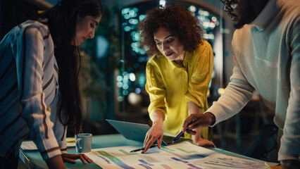Fototapeta premium Team of Young Excited Colleagues Making a Group Meeting in Conference Room in Creative Agency. Diverse Managers Using Laptop Computer, Discussing a New Corporate Strategy. Evening at Work.