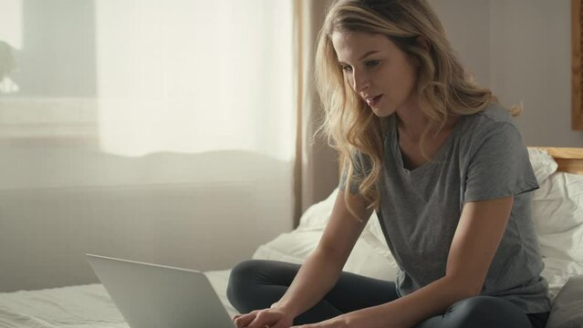 Caucasian woman sitting on the bed and using the laptop at morning. Shot with RED helium camera in 8K. 