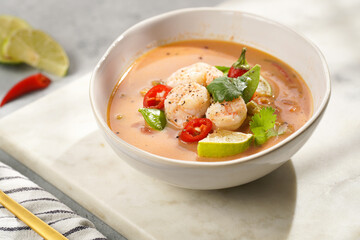 a spicy thai coconut soup or curry made of coconut milk, cherry tomatoes, snow pea, chili pepper, lime, ginger, shrimps and fresh cilantro on marble board on grey concrete background