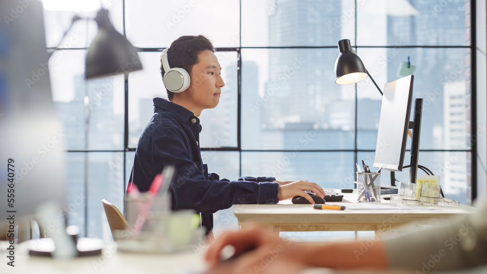 Poster young asian man working on a computer and listening through headphones in a modern office. male clie