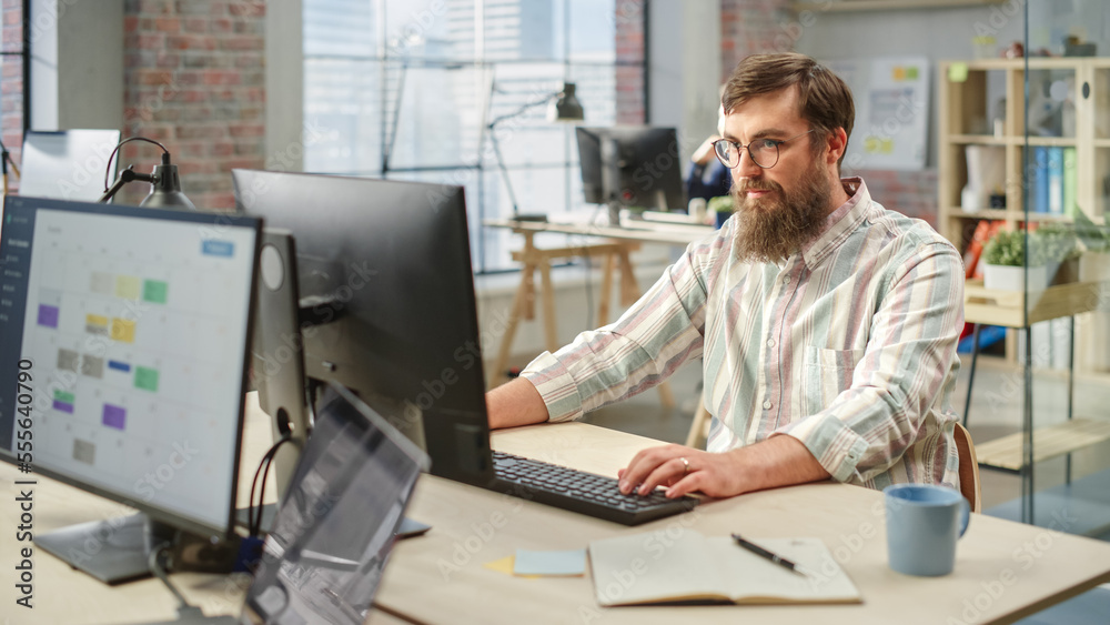 Poster Portrait of Creative Bearded White Man with Glasses Focused While Using Computer in Bright Spacious Office. Marketing Manager Building a New Strategy.