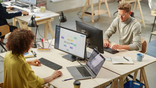 Group of Diverse Multiethnic Young Creative Colleagues Working On Computers in Modern Office. Biracial Female Team Lead Managing a Work Project that is Displayed on Screen. Young White Man Typing.