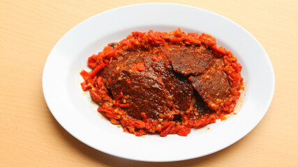 Dendeng balado or jerky beef with spicy seasoning is a traditional cuisine from west sumatera, indonesia. it is made from slice of beef with spicy sauce called sambal. served on plate.