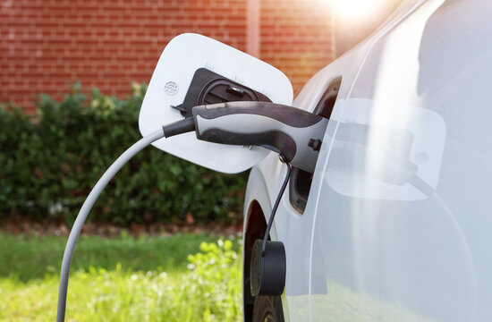 Nahaufnahme eines Steckers beim Laden eines Elektroautos im Gegenlicht vor roter Wand