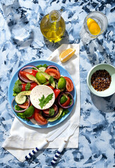 Greek salad in a restaurant serving on a black board with olive oil. The salad contains cucumbers, tomatoes, lime, cheese, onions, herbs, spices and lemon. Olive oil salad dressing.