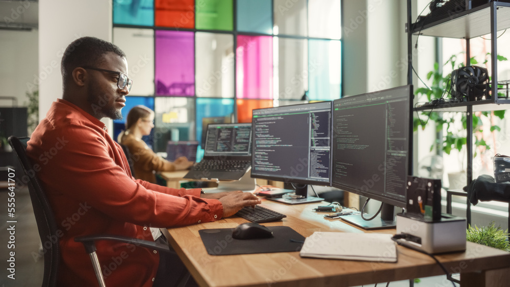 Aufkleber Black Man Writing Lines of Code On Desktop PC With Two Monitors and a Laptop Aside in Stylish Office. Professional Male Developer Programming Artificial Intelligence Software for Start-Up Company.