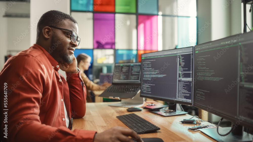 Poster Black Man Writing Lines of Code On Desktop PC With Two Monitors and a Laptop in Stylish Office. Professional Male Developer Programming Artificial Intelligence Software for Start-Up Company.
