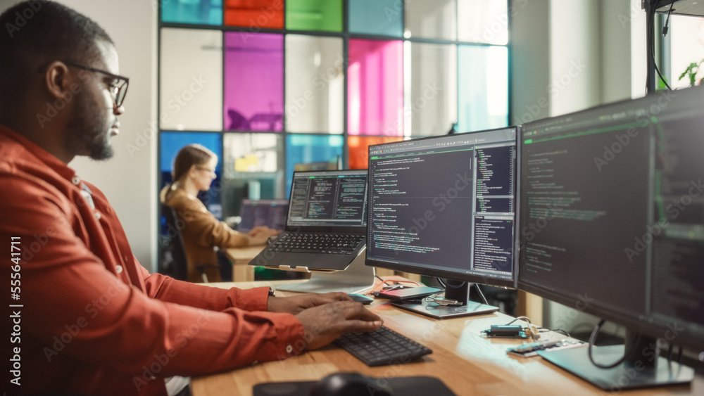 Fototapete African American Man Writing Code on Desktop Computer With Multiple Monitors Set Up and a Laptop in Creative Office. Professional Data Scientist Using Software to Analyze Information From Internet.
