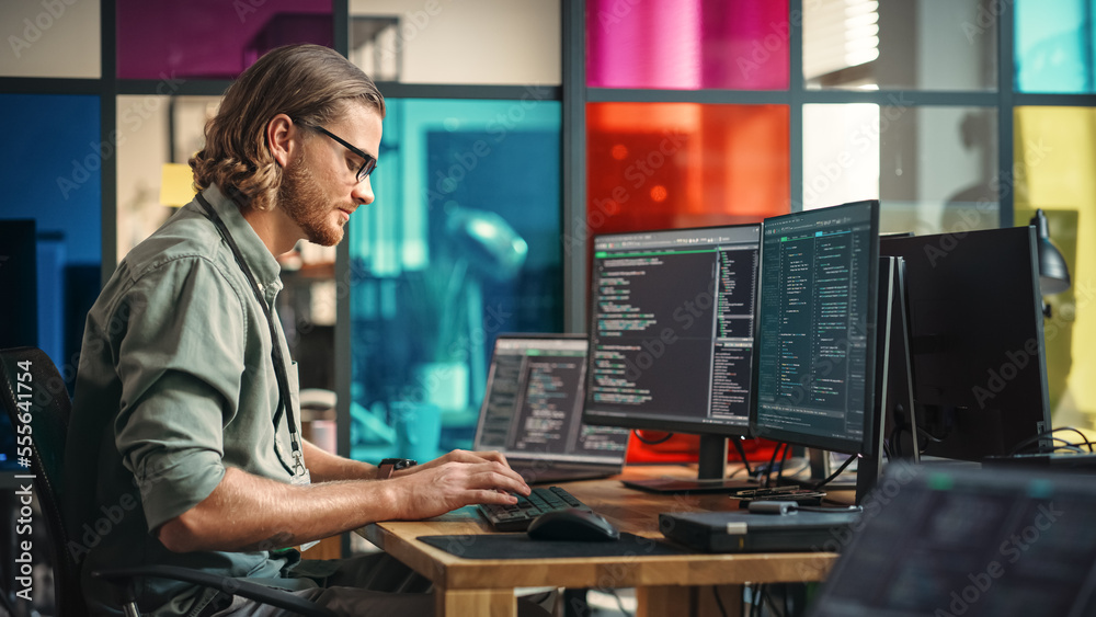 Leinwandbilder Male Programmer Writes Code On Desktop Computer With Multiple Monitor Setup And a Laptop Aside In Creative Office. Caucasian Man Developing Mobile App For Innovative Tech Start-Up Online Service.