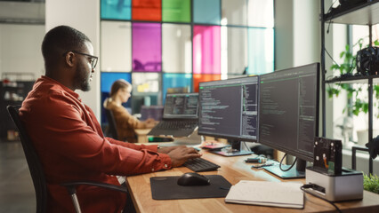African American Man Coding on Desktop Computer with Professional Multiple Monitors Setup in Creative Office. Male Software Engineer Developing Mobile Application for Innovative Start-Up Company.