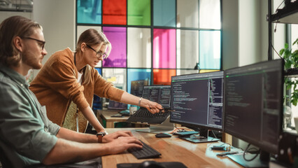 Female Senior Software Engineer Gives Advice to Male Junior Developer, Pointing at Desktop Computer Display With Code. Caucasian Woman Offers New Features, Helps Fixing Bugs in Modern SaaS Platform.