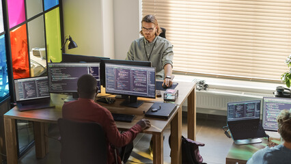 Diverse Colleagues Writing Code on Desktop Computers With Professional Multiple Monitors Setup. Software Development Team Working on Software as a Service Platform For Business Clients.