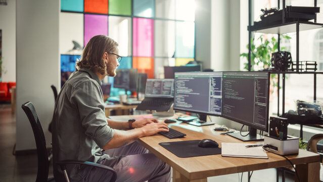 Professional Male Programmer Writing Code on Desktop Computer With Multiple Displays in Stylish Office. Caucasian Man Does Data Scraping For Artificial Intelligence Innovative Tech Start-Up.