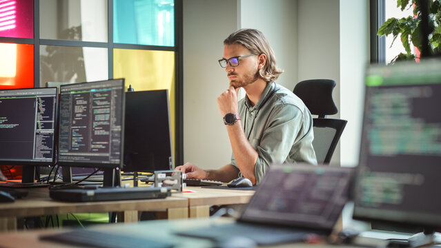 Focused Caucasian Man Coding On Desktop Computer in Stylish Office Space. Male Software Engineer Developing Innovative Application For Business Customers in Technological Start-up Company.