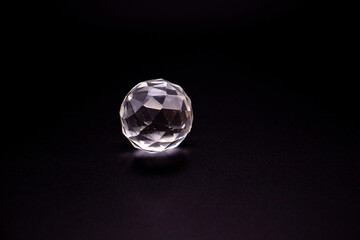 Faceted sphere, sparkling crystal on dark, black background. Large glass with light refraction, stone backdrop. Empty space for inscriptions