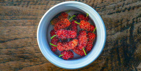 Top view of bright red mulberry fruit in a bowl on wooden background, Healthy fresh mulberry fruit