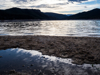 imagen de los reflejos del sol sobre un pantano, con las montañas de fondo y el cielo azul con nubes