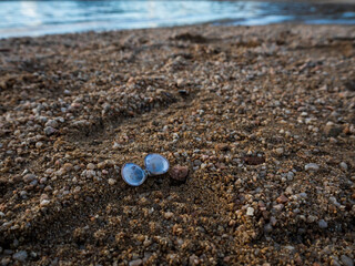imagen detalle de una concha abierta entre piedras de distinto tamaño y una huella de zapato en la arena