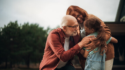 Grandfather and Grandmother are Happy to Meet Their Granddaughter in Front of their Suburbs House. Grandparents Hugging the Girl, Enjoying Family Time with Grandchild.