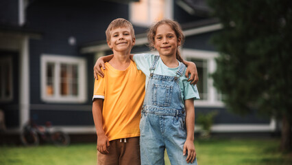 Young Happy Brother and Sister Standing in Front of a Country House, Embracing Each Other, Looking at Camera and Smiling. Two Kids Enjoying Childhood and Friendship.