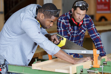 men using hand saw to cut wood in a woodshop