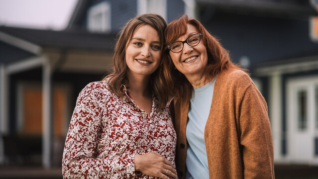 Portrait of a Cheerful Beautiful Female Standing Together with Her Senior Mother or Grandparent. Young Woman is Pregnant and Expecting a Baby. Family Members Embrace, Smile and Look at Camera.