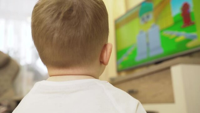 A little boy sits and watches cartoons on TV, shooting from behind the child. The picture on the TV is blurry.