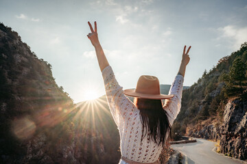 Fototapeta premium Traveler woman in brown hat and white sweater looking at amazing mountains and forest, wanderlust travel concept, atmospheric epic moment