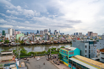 Obraz premium HO CHI MINH, VIETNAM - December 3, 2022: Slum wooden house on the Saigon river bank, in front of modern buildings in ho chi minh city. View to district 1, see Bitexco tower, Landmark 81.