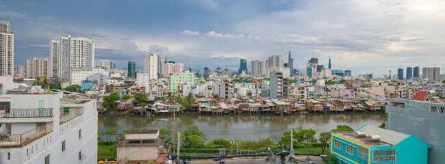 Fototapeta na wymiar HO CHI MINH, VIETNAM - December 3, 2022: Slum wooden house on the Saigon river bank, in front of modern buildings in ho chi minh city. View to district 1, see Bitexco tower, Landmark 81.