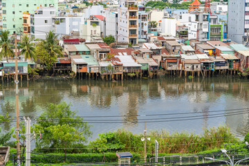 Fototapeta na wymiar HO CHI MINH, VIETNAM - December 3, 2022: Slum wooden house on the Saigon river bank, in front of modern buildings in ho chi minh city. View to district 1, see Bitexco tower, Landmark 81.
