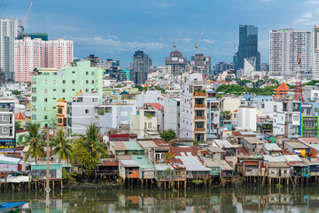 HO CHI MINH, VIETNAM - December 3, 2022: Slum wooden house on the Saigon river bank, in front of modern buildings in ho chi minh city. View to district 1, see Bitexco tower, Landmark 81.