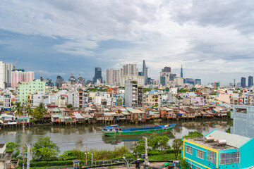 Obraz premium HO CHI MINH, VIETNAM - December 3, 2022: Slum wooden house on the Saigon river bank, in front of modern buildings in ho chi minh city. View to district 1, see Bitexco tower, Landmark 81.
