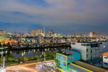 HO CHI MINH, VIETNAM - December 3, 2022: Slum wooden house on the Saigon river bank, in front of modern buildings at night in ho chi minh city. View to district 1, see Bitexco tower, Landmark 81.