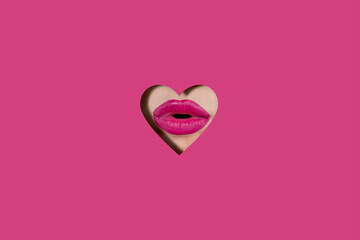 A girl with beautiful plump lips, painted pink lipstick. Lips in a hole in the form of a heart made...