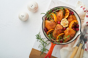 Baked chicken thighs with orange, cranberry and spicy herbs rosemary servered in frying pan on light background. Festive Christmas Dinner Concept menu. Top view. copy space
