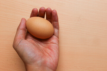 Hand holding chicken egg isolated on brown wooden background