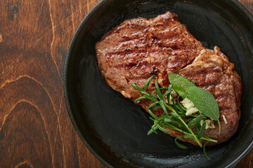Steaks. Sliced grilled meat steak New York or Ribeye with spices rosemary and pepper in iron pan black on marble board on old wooden background. Top view. Mock up.