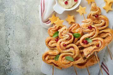 Christmas or New Year appetizer. Christmas tree shape puff pastry buns with cheese and ham. Group of Christmas tree shapes on marble stand. Festive idea for Christmas or New Year dinner. Top view.
