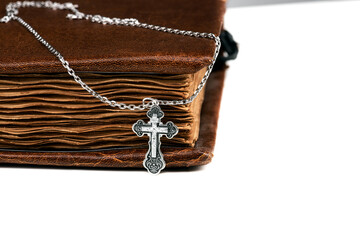 isolated on a white background jewelry silver cross on a chain with a shadow lies on an old book