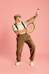 Portrait of senior, old man in stylish classical clothes posing with racket, over pink background. Illusion of guitar