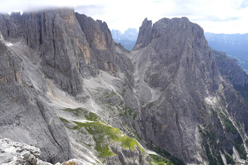 Grey huge rocks of Italian Dolomites with trolls paths. Green grass and trees around them. Summertime