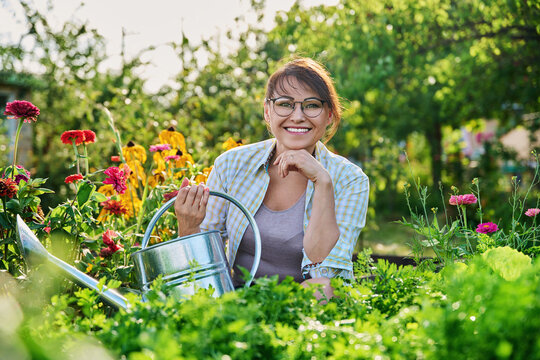 Middle-aged woman with watering can near garden bed with spicy fragrant herbs