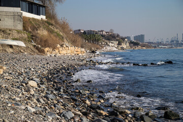 waves crashing on the beach covered with shells and round stones industrial structures in the distance harbor and cranes