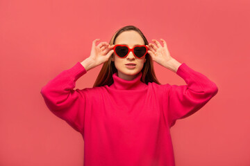Stylish girl holding black and red heart shaped glasses and wearing pink outfit isolated on colored pink background.

St Valentines Day, International Womens Day or lifestyle concept.