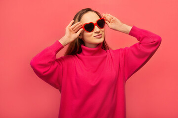 Stylish happy cheerful girl wearing pink sweater with red heart shaped glasses and looking up...