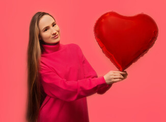 Happy young woman in pink knitted dress holding red heart shaped air balloon and looking at camera isolated on pink background.

St Valentine's Day, March 8, Women's Day, Mother's Day or love concept.