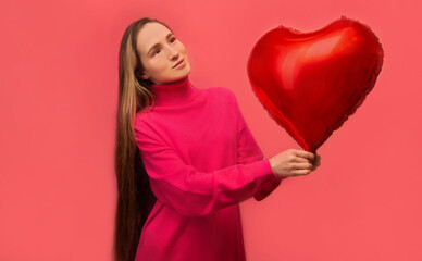 Dreaming stylish young woman holding red heart shaped air balloon and looking up isolated on pink background.

Saint Valentines Day, International Womens Day or happy birthday celebration concept.