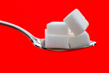 Sugar cubes in a spoon on red background